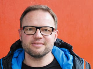 Mann mit blauer Kapuze und Brille vor rotem Hintergrund. Mann mit blauer Kapuze und Brille vor rotem Hintergrund.