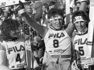 Schwarz-Weiss Fotografie mit den drei besten Riesenslalom-Fahrerinnen in Siegespose, im Renndress mit Startnummern und Skiern.