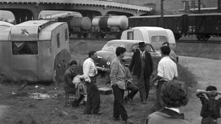 Wohnwagen und eine Gruppe von Männern stehen neben Gleisen. Wohnwagen und eine Gruppe von Männern stehen neben Gleisen.