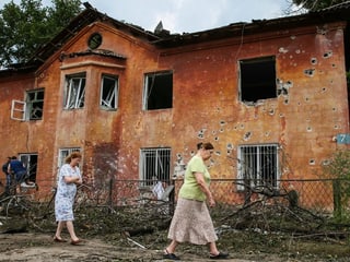 Frauen spazieren an einem durchlöcherten Haus vorbei