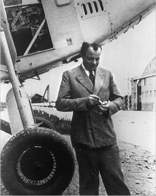Schwarzweissbild: Saint-Exupéry im Anzug vor einem Flugzeug.