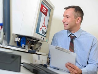 Ein Mann schaut lachend auf einen Computerbildschirm, auf dem das PDF-Logo zu sehen ist.
