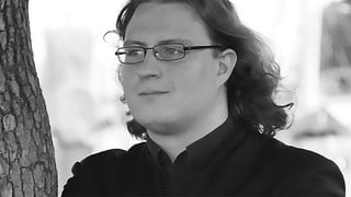 Schwarz-Weiss-Fotografie von einem Mann mit schulterlangen Haaren und Brille.