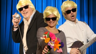 Moderatoren mit blonder Heino Perücke und dunkler Sonnenbrille, Microphon, Gitarren und Filzblumen.