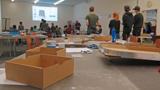 Gruppenraum mit Kartonschachteln im Vordergrund und jungen Menschen im Hintergrund. Gruppenraum mit Kartonschachteln im Vordergrund und jungen Menschen im Hintergrund.