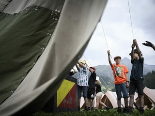 Junge Pfadfinderinnen und Pfadfinder hängen eine Plane am Lagerplatz auf dem Zeltplatz auf. 
