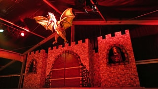 Bühnenbild aus Burg mit lebensechtem Drachen aus Pappmaché im Scheinwerferlicht