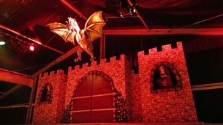 Bühnenbild aus Burg mit lebensechtem Drachen aus Pappmaché im Scheinwerferlicht Bühnenbild aus Burg mit lebensechtem Drachen aus Pappmaché im Scheinwerferlicht