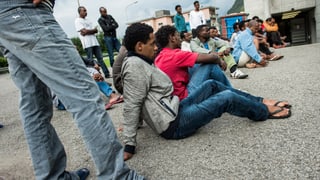 Eritreer sitzen auf einem asphaltierten Vorplatz vor einer Zivilschutzanlage.