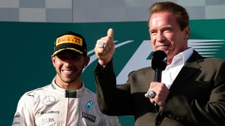 Lewis Hamilton steht neben Arnold Schwarzenegger, der den rechten Daumen in die Luft reckt.