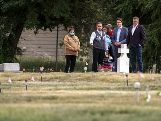 Trudeau und weitere Personen stehen vor einem Friedhof mit Fähnchen und Kreuzen.