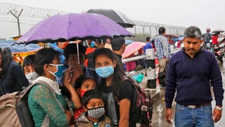 Menschen mit Schutzsmaske unter Schirm.