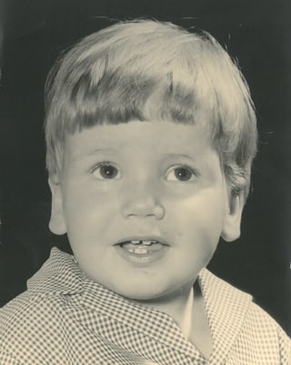 Porträtfoto von einem kleinen jungen mit einem Pagenschnitt und grossen dunklen Augen.
