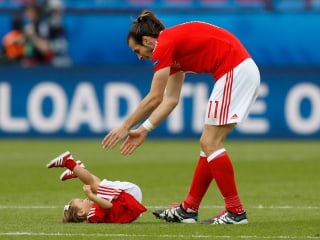 Bale im Trikot auf Platz mit Tochter, liegend am Boden