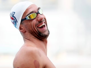 Michael Phelps lacht mit Badekappe im Wasser.