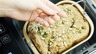 Eine Frau hebt ein fertiges Brot aus einem Backautomaten.