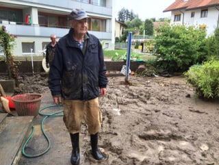 Ein älterer Mann steht in seinem Garten voller Schlamm.