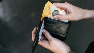 Eine Hand nimmt zwei 10-Franken-Scheine aus einem Portemonnaie.