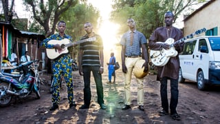 Vier Männer stehen in Mali auf einem holprigen Weg. Die Sonne scheint ihnen in den Rücken, sie halten ihre Instrumente in den Händen.