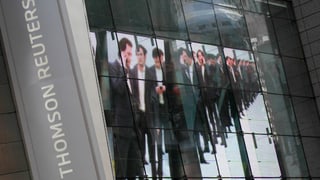 Thomson-Reuters-Logo, daneben ein Werbeplakat mit Businessmännern. Thomson-Reuters-Logo, daneben ein Werbeplakat mit Businessmännern.