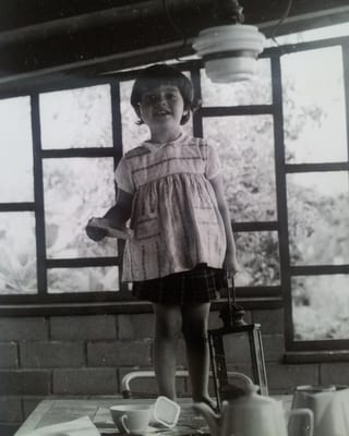 Ein kleines barfüssiges Mädchen steht mit einer Laterne und einem Zettel in der Hand auf einem Tisch.