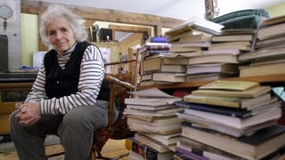 Grace Plaey sitzt in ihrem Zuhause neben einem Stapel Bücher.
