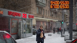 Mann überquert die Strasse, im Hintergrund digitale Anzeige von Währungskursen.