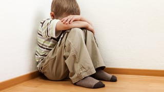 Ein Kind sitzt in einer Ecke, den Kopf zwischen den Armen vergraben. Ein Kind sitzt in einer Ecke, den Kopf zwischen den Armen vergraben.