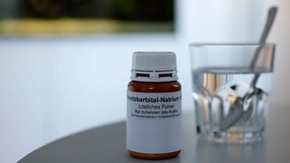 Symbolbild: Eine Medikamentendose, angeschrieben mit Pentobarbital Natrium, daneben steht ein Glas Wasser mit einem Löffel.