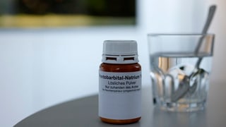 Symbolbild: Eine Medikamentendose, angeschrieben mit Pentobarbital Natrium, daneben steht ein Glas Wasser mit einem Löffel. Symbolbild: Eine Medikamentendose, angeschrieben mit Pentobarbital Natrium, daneben steht ein Glas Wasser mit einem Löffel.