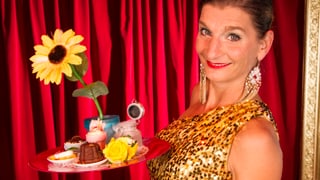 Marion Gasser in goldenem Kleid mit roten Lippen und einem Teller voller Küchlein.
