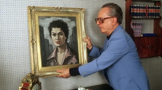 ein älterer Mann hängt ein Porträt einer Frau auf