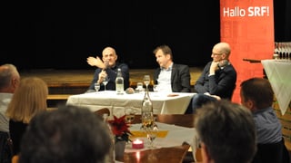 Drei Männer sitzen an einem Tisch. Im Hintergrund das Hallo SRF Logo