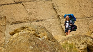 Reese Witherspoon mit riesigem Rucksack vor grosser Felswand.