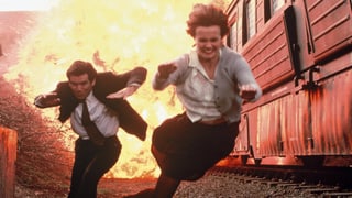 Ein Mann und eine Frau rennen aus einem explodierenden Hochsicherheitszug.