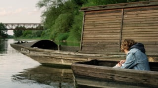 Ein Knabe sitzt auf einem Fluss in einem Holzboot.