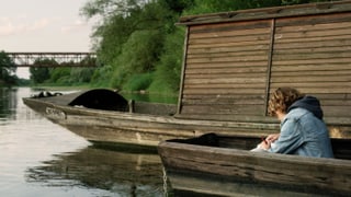 Ein Knabe sitzt auf einem Fluss in einem Holzboot. Ein Knabe sitzt auf einem Fluss in einem Holzboot.