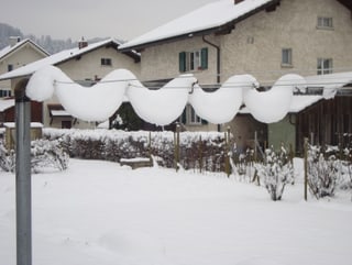 Eine Wäscheleine in einem Hinterhof. Als läge eine Decke über die Leine, hängt der Schnee zwischen den einzelnen Leinen durch.