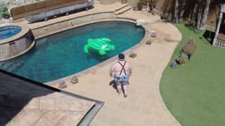 Ein dicker Mann in Badehose schreitet auf einen Pool zu, in dem eine aufgeblasene Schildkröte liegt.