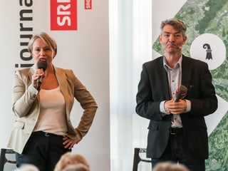 Schneider mit Mikrofon und Kohler vor Plakaten.