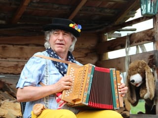 Hans Frischknecht mit Sennerhemd und Blumen geschmückten Hut spiele Schwyzerörgeli.