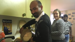 Ein Mann mit einer Pfanne voll Reis steht in einer Küche, daneben eine Frau.