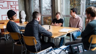 Fünf Männer sitzen in einem Schulzimmer um einen Tisch. Fünf Männer sitzen in einem Schulzimmer um einen Tisch.