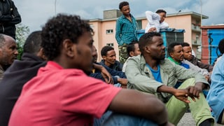 Männer aus Eritrea sitzen auf dem Boden vor einer Zivilschutzanlage.