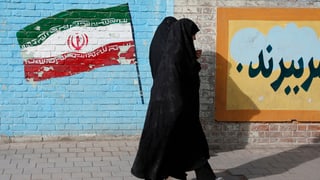 Zwei Frauen gehen an einer Wand mit einer aufgemalten iranischen Flagge vorbei.
