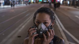 Junge Frau mit Gasmaske auf nächtlicher Hongkonger Strasse.