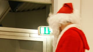 Ein Weihnachtsmann, aufgenommen von hinten, geht Richtung Notausgang.