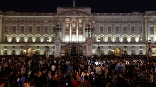 Beleuchteter Buckingham Palace am Abend, davor eine Menschenmasse. Beleuchteter Buckingham Palace am Abend, davor eine Menschenmasse.