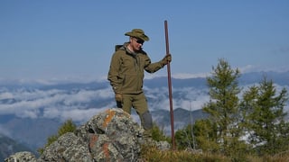 Putin in grüner Outdoorkleidung mit Stock vor blauem Himmel. Putin in grüner Outdoorkleidung mit Stock vor blauem Himmel.