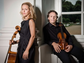 Ein Frau mit Cello stehend, ein Mann mit Violine sitzend. Ein Frau mit Cello stehend, ein Mann mit Violine sitzend.